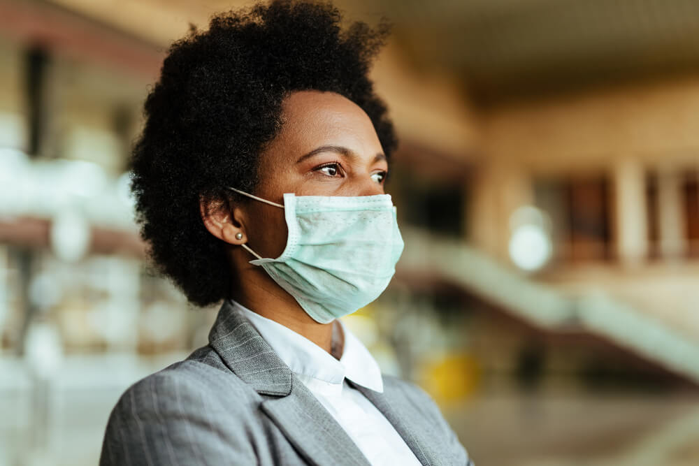Pensive African American businesswoman wearing face mask while waiting at airpor